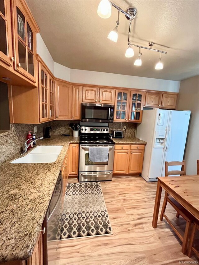 kitchen featuring a textured ceiling, stone countertops, stainless steel appliances, sink, and light wood-type flooring