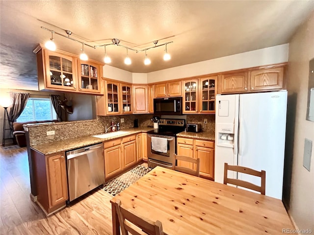 kitchen with light wood-type flooring, stainless steel appliances, sink, dark stone counters, and tasteful backsplash