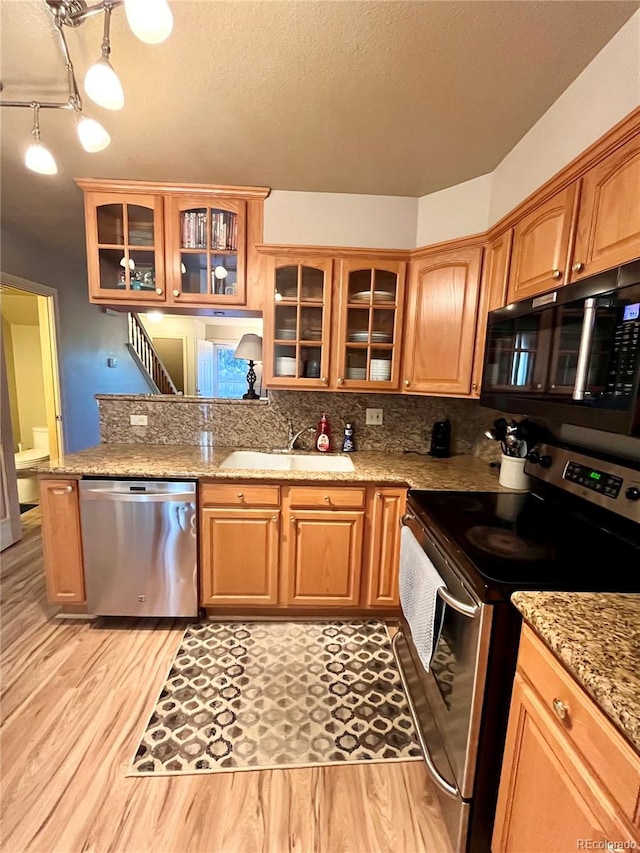 kitchen featuring a textured ceiling, appliances with stainless steel finishes, sink, light stone counters, and light wood-type flooring