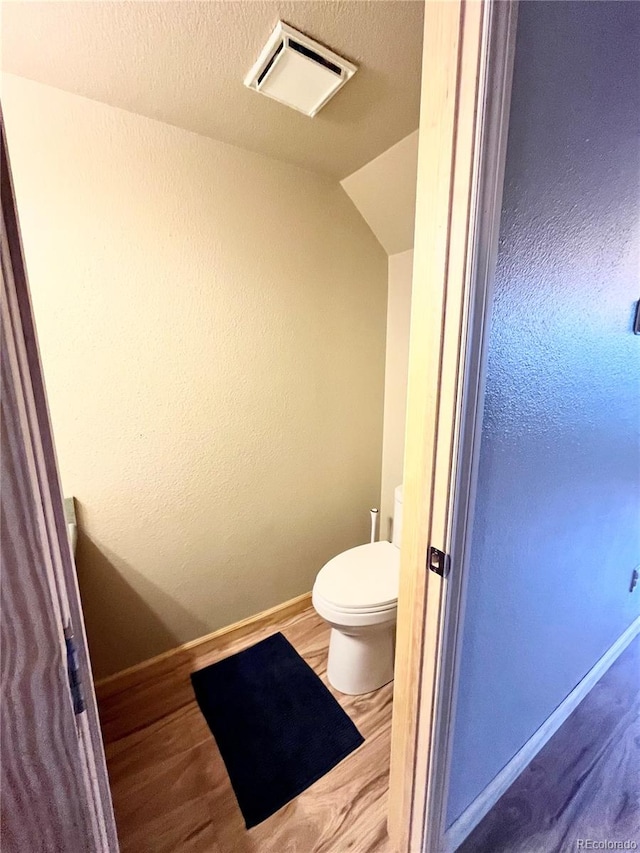 bathroom featuring a textured ceiling, toilet, hardwood / wood-style floors, and lofted ceiling