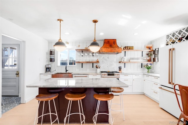 kitchen featuring light wood-style flooring, freestanding refrigerator, custom exhaust hood, open shelves, and a sink