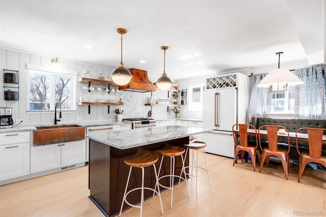 kitchen with a sink, white cabinetry, light wood-type flooring, open shelves, and high end appliances