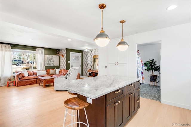 kitchen with dark brown cabinetry, a kitchen breakfast bar, baseboards, hanging light fixtures, and light wood-style floors