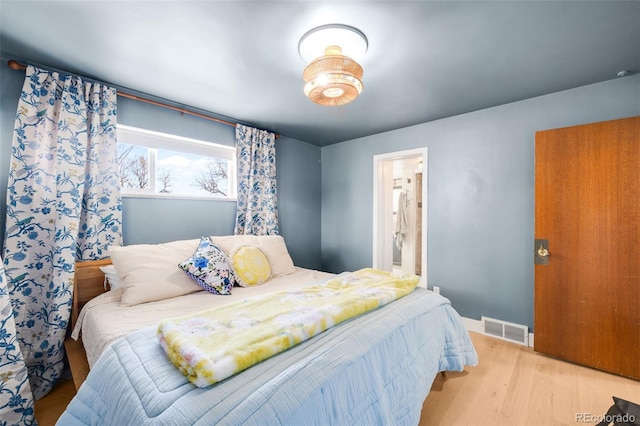 bedroom with ensuite bathroom, wood finished floors, visible vents, and baseboards