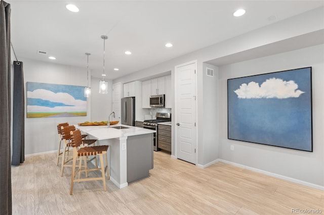 kitchen with an island with sink, white cabinetry, sink, a kitchen bar, and stainless steel appliances