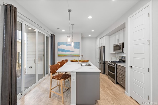 kitchen featuring appliances with stainless steel finishes, pendant lighting, white cabinets, a kitchen breakfast bar, and a kitchen island with sink