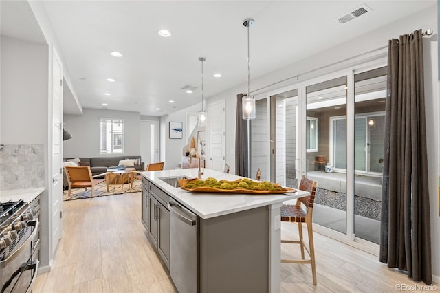 kitchen featuring decorative light fixtures, an island with sink, gray cabinetry, a kitchen breakfast bar, and stainless steel appliances