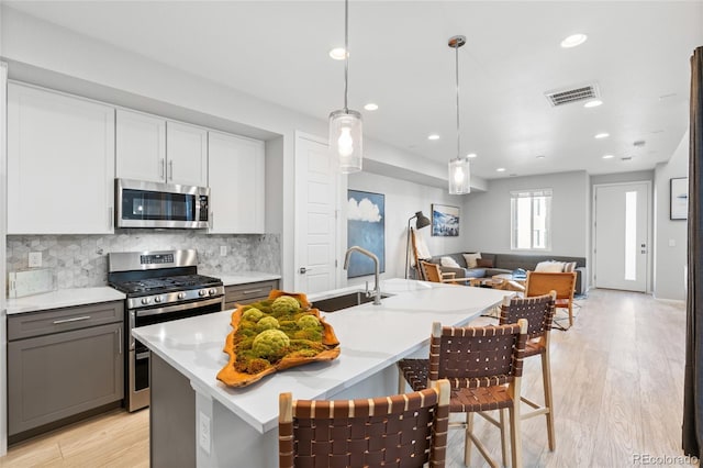 kitchen featuring sink, a center island with sink, pendant lighting, stainless steel appliances, and decorative backsplash