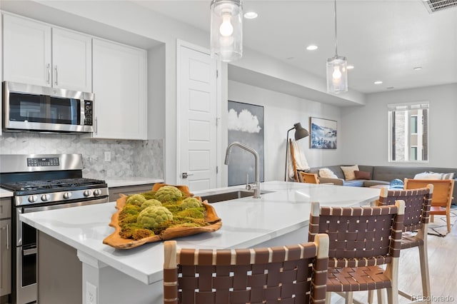 kitchen featuring light wood-style flooring, stainless steel appliances, a sink, visible vents, and backsplash