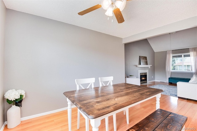 dining space featuring vaulted ceiling, ceiling fan, a textured ceiling, and light wood-type flooring