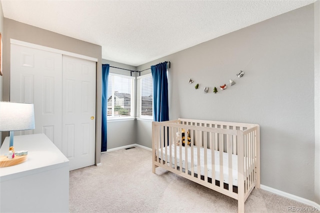 bedroom featuring light colored carpet, a crib, a textured ceiling, and a closet