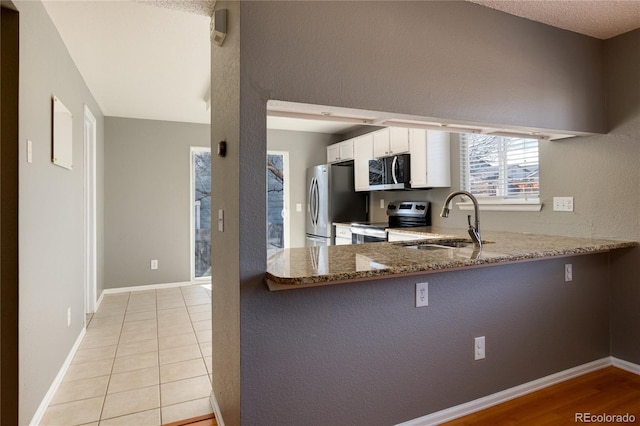 kitchen with kitchen peninsula, stainless steel appliances, sink, dark stone countertops, and white cabinetry