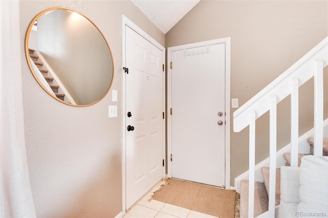 foyer entrance featuring lofted ceiling, a textured ceiling, and light tile patterned floors