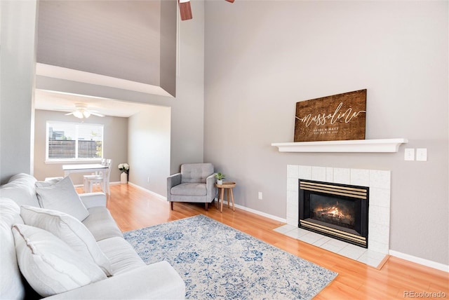 living room with a tile fireplace, wood-type flooring, and ceiling fan