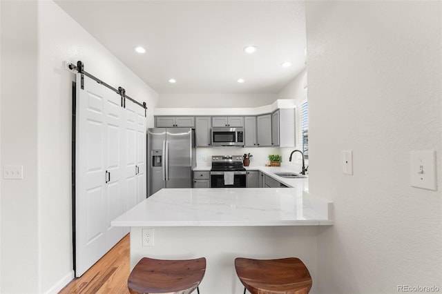 7600 W Coal Mine Ave Unit B, Littleton, CO 80123 - kitchen featuring stainless steel appliances, gray cabinetry, a barn door, a peninsula, and a kitchen breakfast bar