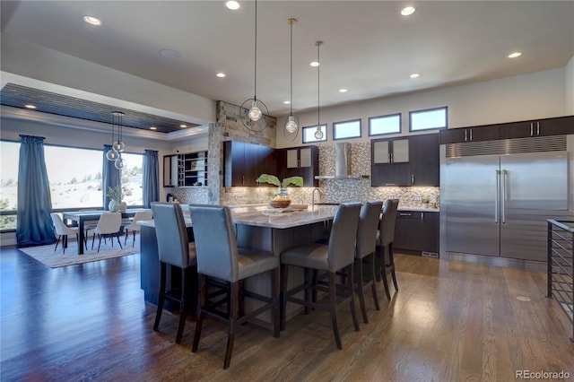 kitchen with dark hardwood / wood-style floors, decorative backsplash, stainless steel built in fridge, and dark brown cabinetry