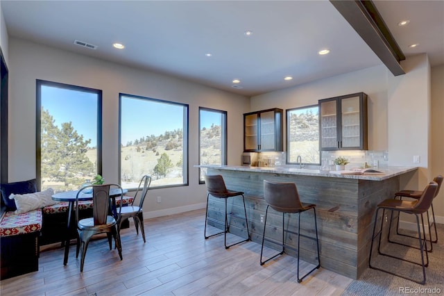 bar featuring light stone countertops, decorative backsplash, sink, light wood-type flooring, and beam ceiling