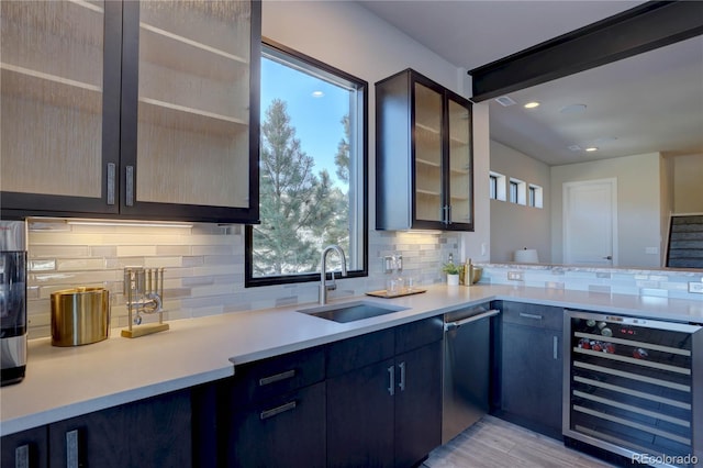 kitchen featuring backsplash, light wood-type flooring, wine cooler, dishwasher, and sink