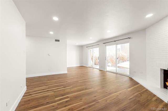 unfurnished living room featuring visible vents, recessed lighting, a brick fireplace, and wood finished floors