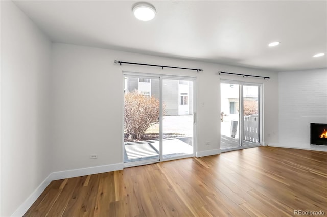 unfurnished living room with a large fireplace, baseboards, light wood-type flooring, and recessed lighting