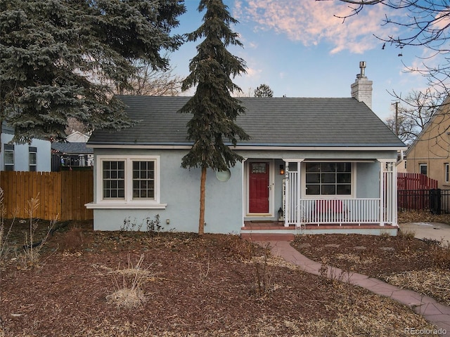 view of front of property featuring a porch, fence, a chimney, and stucco siding