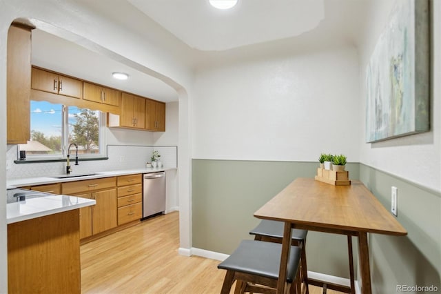 kitchen with a sink, dishwasher, tasteful backsplash, light wood-style flooring, and light countertops