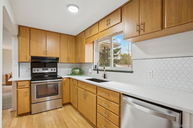 kitchen featuring stainless steel appliances, a sink, under cabinet range hood, and light countertops