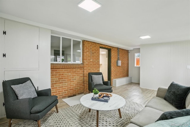 living room featuring light wood-type flooring, brick wall, and baseboards