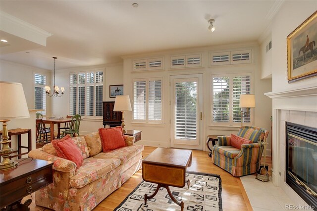 living room featuring ornamental molding, light wood-type flooring, a notable chandelier, and a tile fireplace