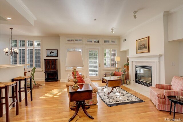 living room with ornamental molding, light hardwood / wood-style floors, a fireplace, and a notable chandelier