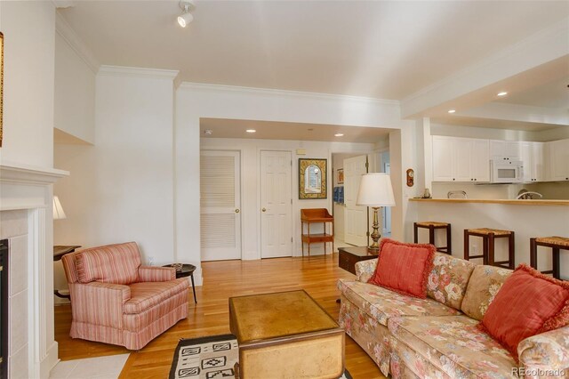 living room featuring light hardwood / wood-style flooring, a tile fireplace, and ornamental molding