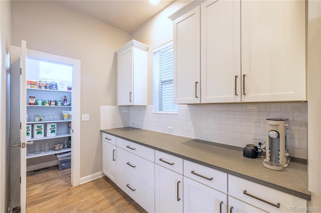 6682 Osage St, Denver, CO 80221 - kitchen with backsplash, white cabinets, light wood-type flooring, dark countertops, and baseboards