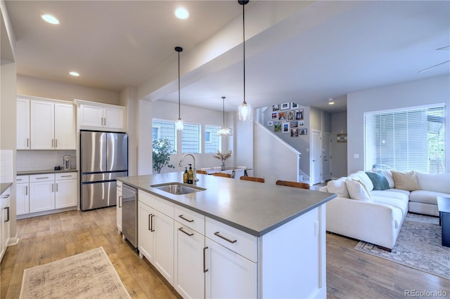 6682 Osage St, Denver, CO 80221 - kitchen with appliances with stainless steel finishes, a sink, light wood finished floors, a kitchen island with sink, and recessed lighting
