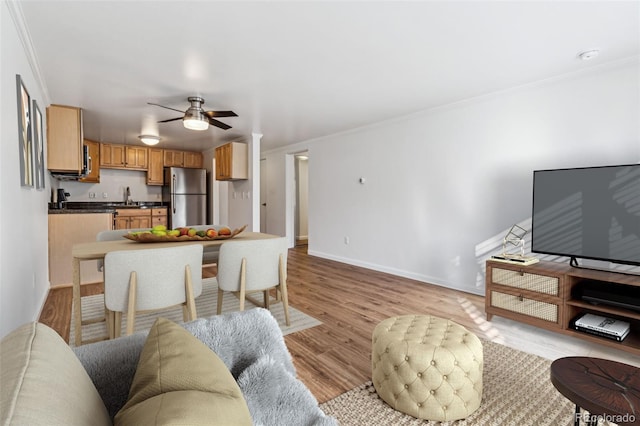 living room featuring ceiling fan, ornamental molding, sink, and light wood-type flooring