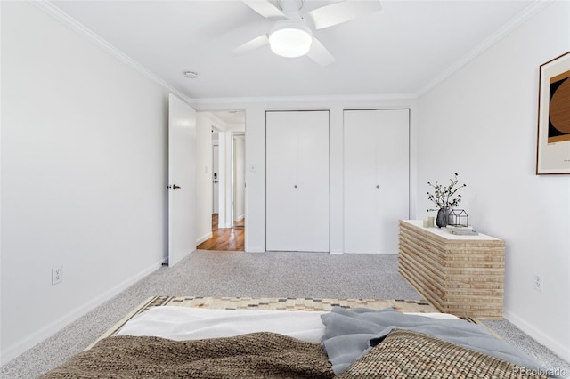 carpeted bedroom featuring ceiling fan, ornamental molding, and multiple closets