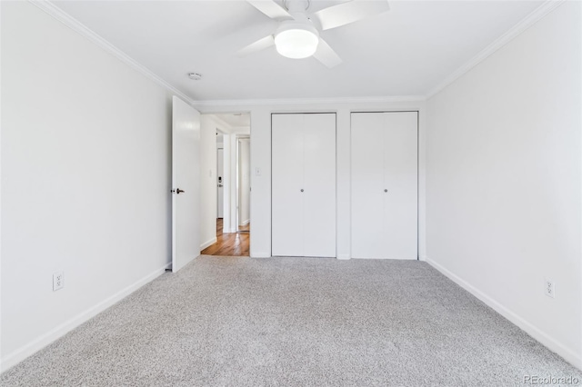 unfurnished bedroom with multiple closets, crown molding, carpet flooring, and ceiling fan