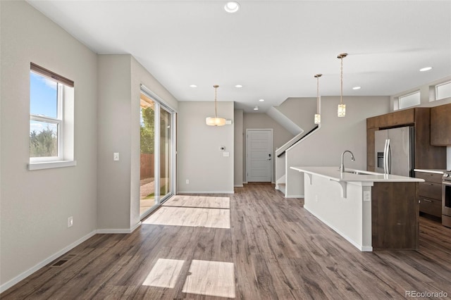 kitchen with an island with sink, hardwood / wood-style flooring, a breakfast bar area, hanging light fixtures, and appliances with stainless steel finishes