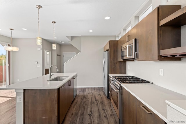 kitchen featuring a kitchen island with sink, stainless steel appliances, dark wood-type flooring, sink, and hanging light fixtures