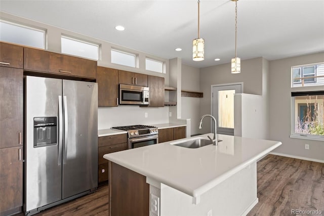 kitchen with dark hardwood / wood-style floors, decorative light fixtures, sink, an island with sink, and appliances with stainless steel finishes