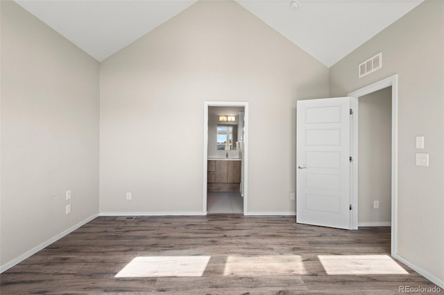 unfurnished bedroom with ensuite bathroom, high vaulted ceiling, and hardwood / wood-style flooring