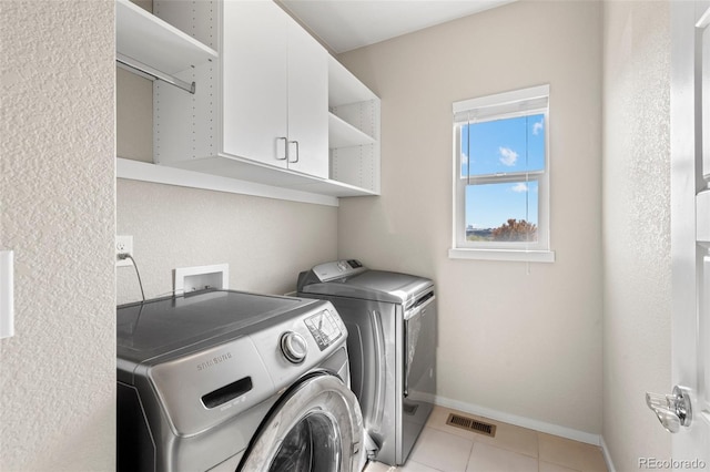 laundry area featuring independent washer and dryer, light tile patterned floors, and cabinets