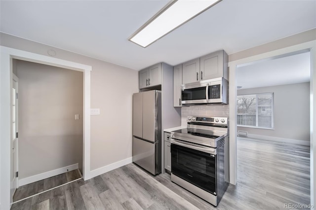 kitchen with backsplash, appliances with stainless steel finishes, light hardwood / wood-style floors, and gray cabinetry