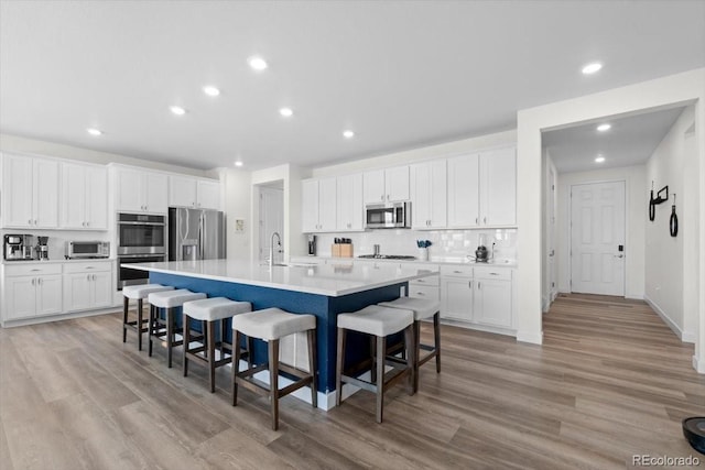 14601 Hudson St, Thornton, CO 80602 - kitchen with stainless steel appliances, backsplash, a large island with sink, light wood-type flooring, and recessed lighting