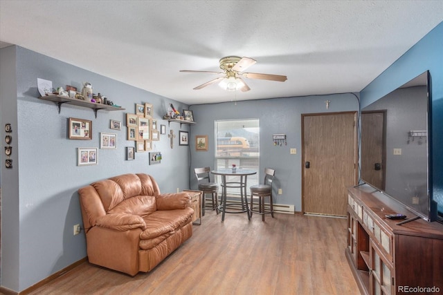 living area with baseboard heating, ceiling fan, hardwood / wood-style floors, and a textured ceiling