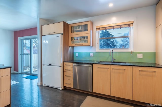 kitchen with dark stone counters, a sink, freestanding refrigerator, dishwasher, and glass insert cabinets