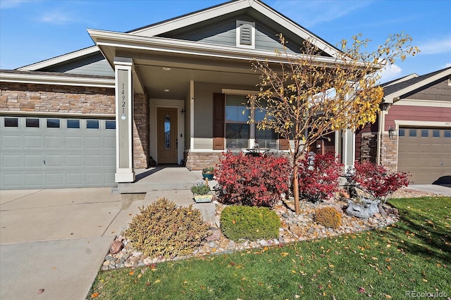 view of front facade with an attached garage, stone siding, a porch, and concrete driveway