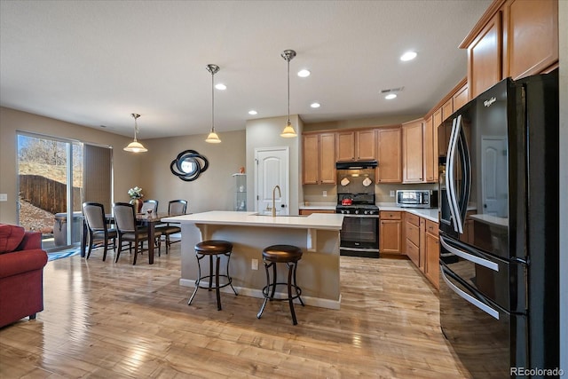 kitchen with pendant lighting, light countertops, a sink, an island with sink, and black appliances