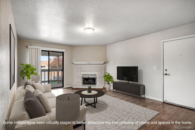 living room featuring a textured ceiling, wood finished floors, baseboards, and a tile fireplace