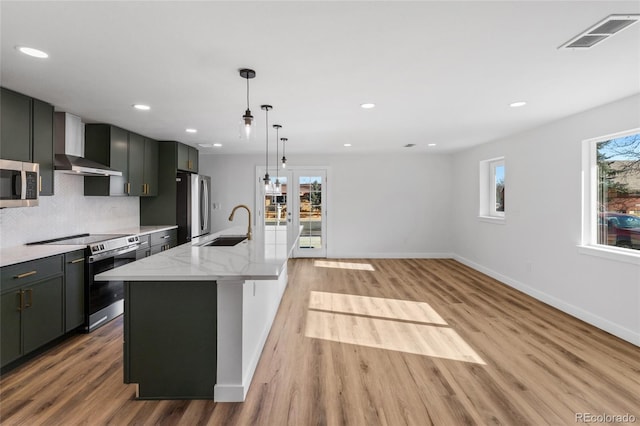 kitchen featuring appliances with stainless steel finishes, sink, light wood-type flooring, backsplash, and a center island with sink