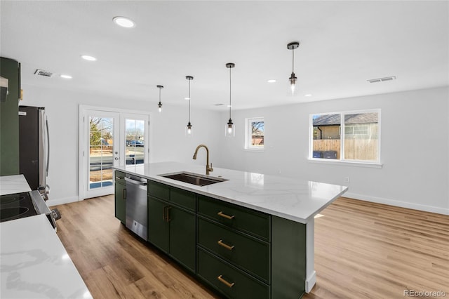 kitchen featuring pendant lighting, appliances with stainless steel finishes, sink, light stone countertops, and a kitchen island with sink